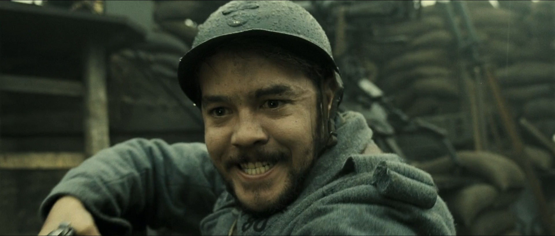 A helmeted soldier smiles in a wet woodland rendered in neighbouring olive, green and blue-grey hues.
