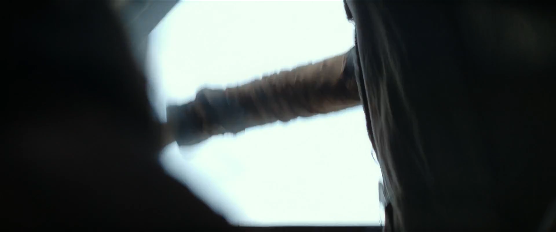 A dark, nearly monochrome close-up catches a blurred metal edge and a shadowed figure against white sky.