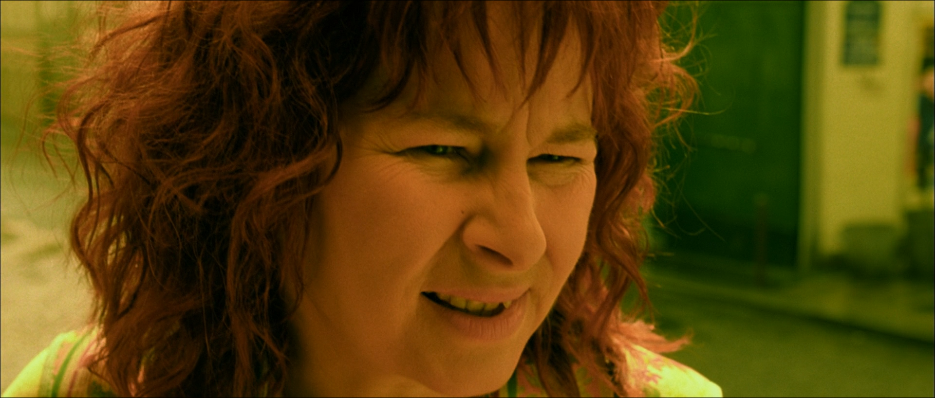 Close-up of a curly-haired woman screwing up her face in laughter, skin, hair and background all washed into one yellow-green.