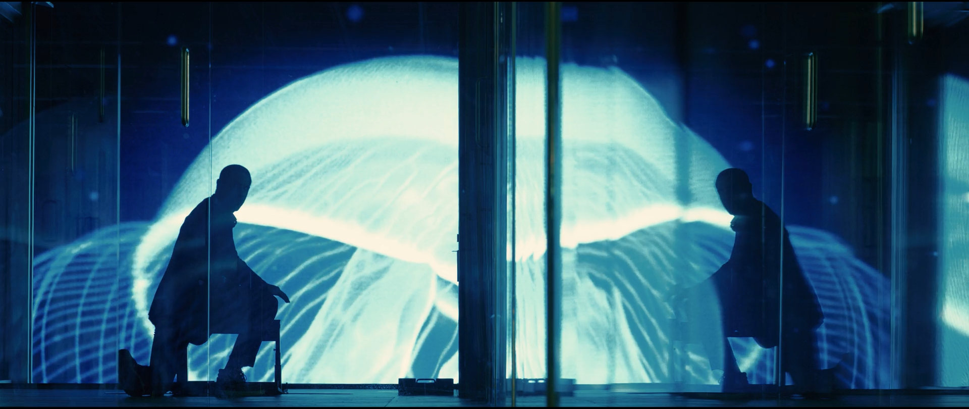 Shot 0908 from Skyfall at 01:47:32:01. An animated jellyfish fills the glass wall in cyan and white and reduces both men to flat black cut-outs; the reflection at right doubles the composition.