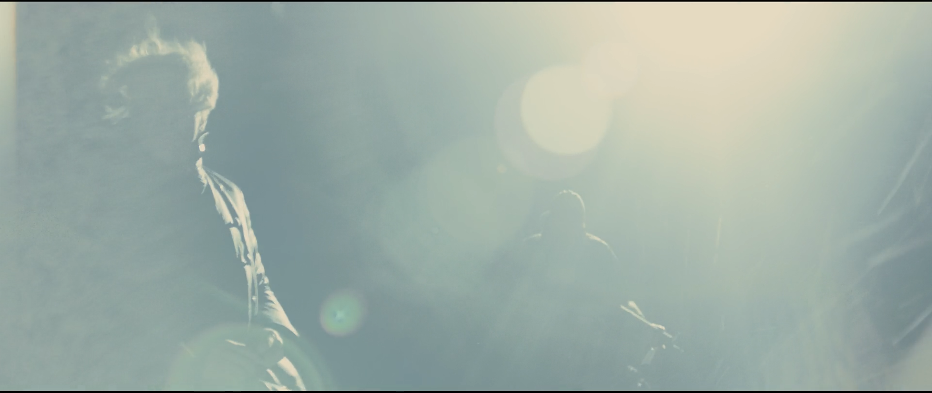 Shot 2314 from Skyfall at 03:01:20:20. Backlit smoke floods the frame to near-white with a cold cast; two figures and a weapon survive as soft grey shapes, and lens flare breaks the light into discs.