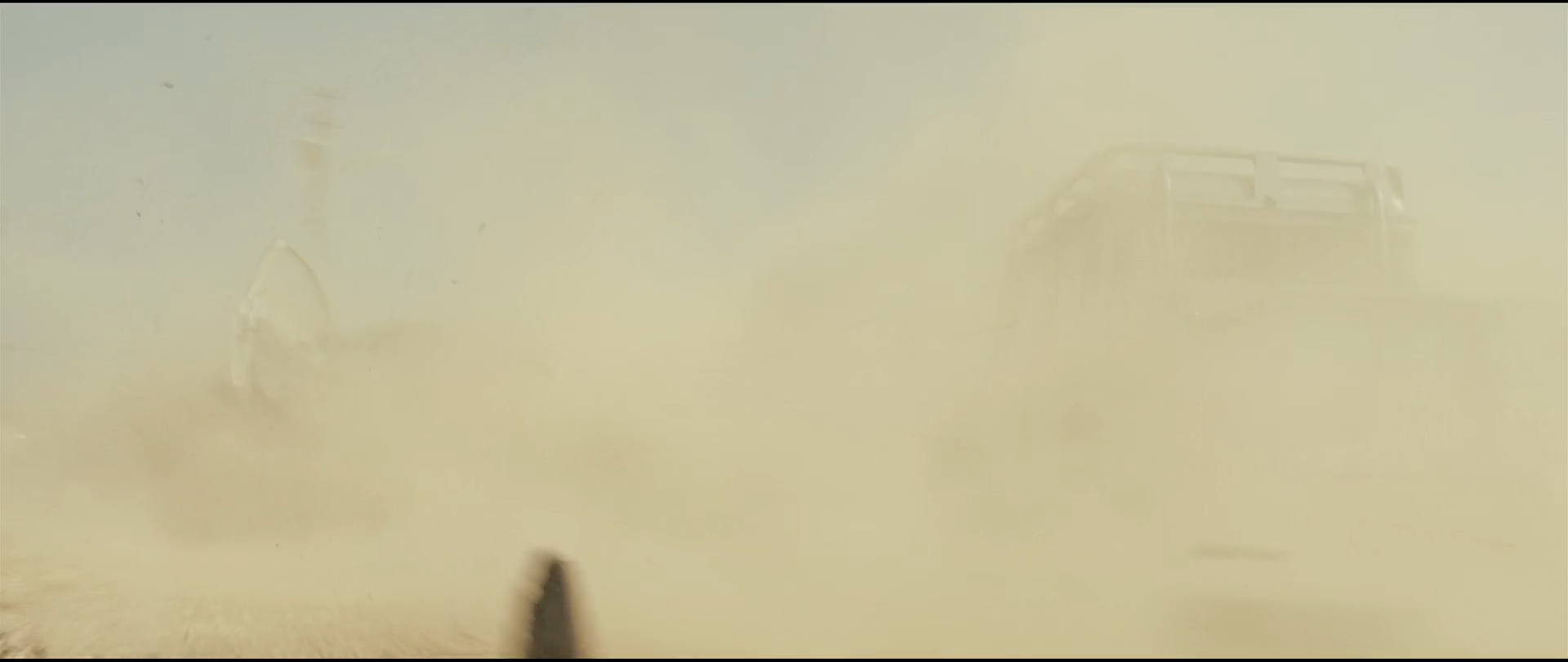 Shot 0301 from Skyfall at 01:08:18:01. Raised dust flattens the field to a single pale sand tone; the truck at right and a small dark shape below survive only as soft edges, with very little chroma anywhere.