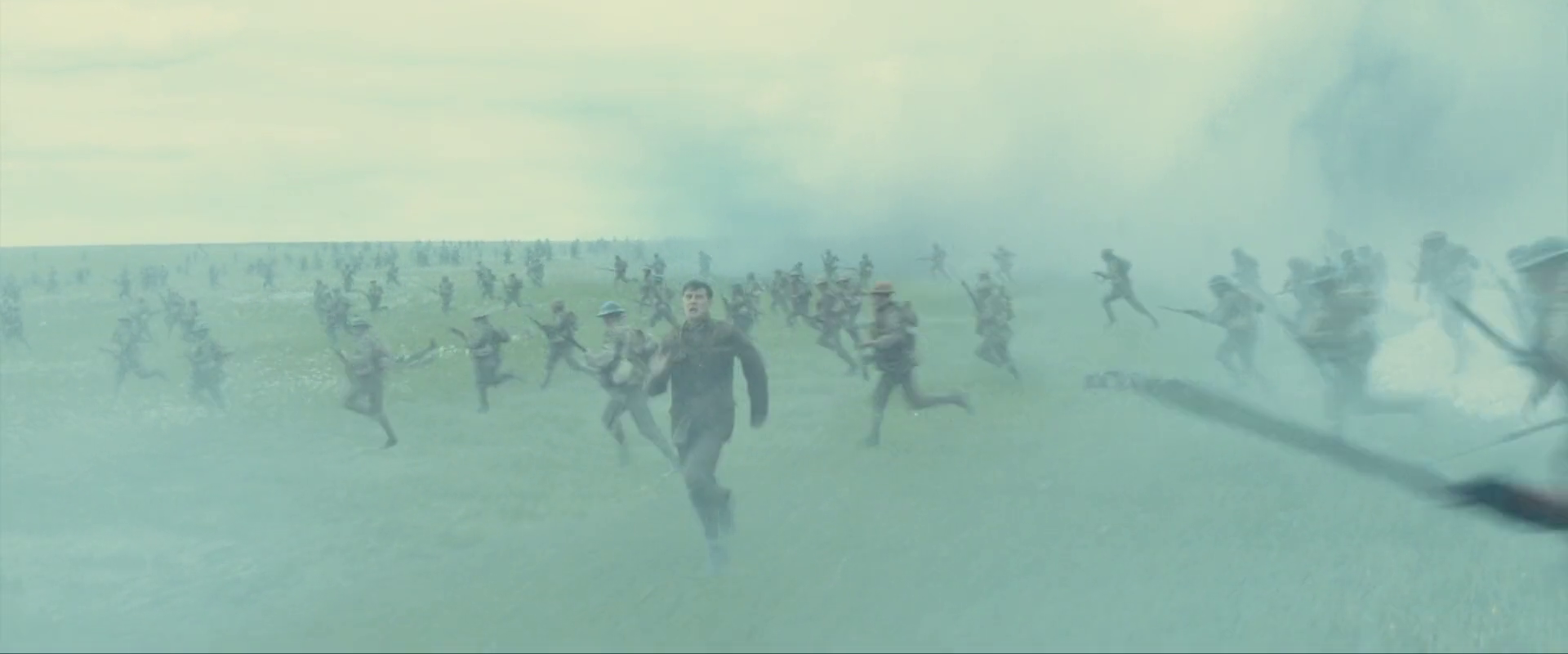 Sample 2930 from 1917 at 1:37:44. Ranks of running men cross from right to left while one figure cuts against them; smoke holds the whole image inside a narrow pale band with very little tonal separation.