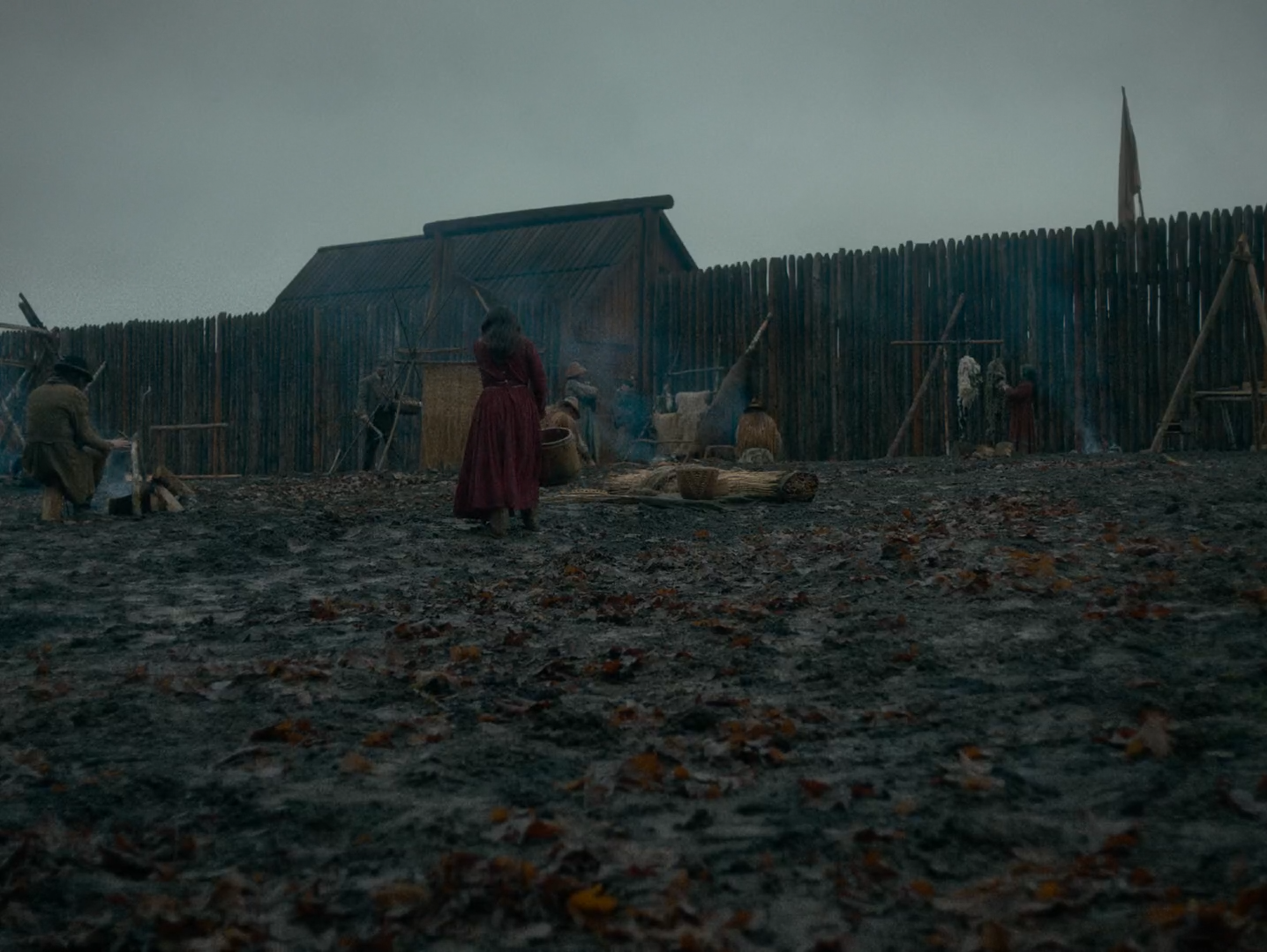 A fort compound of churned mud and a timber palisade under a flat pale sky.