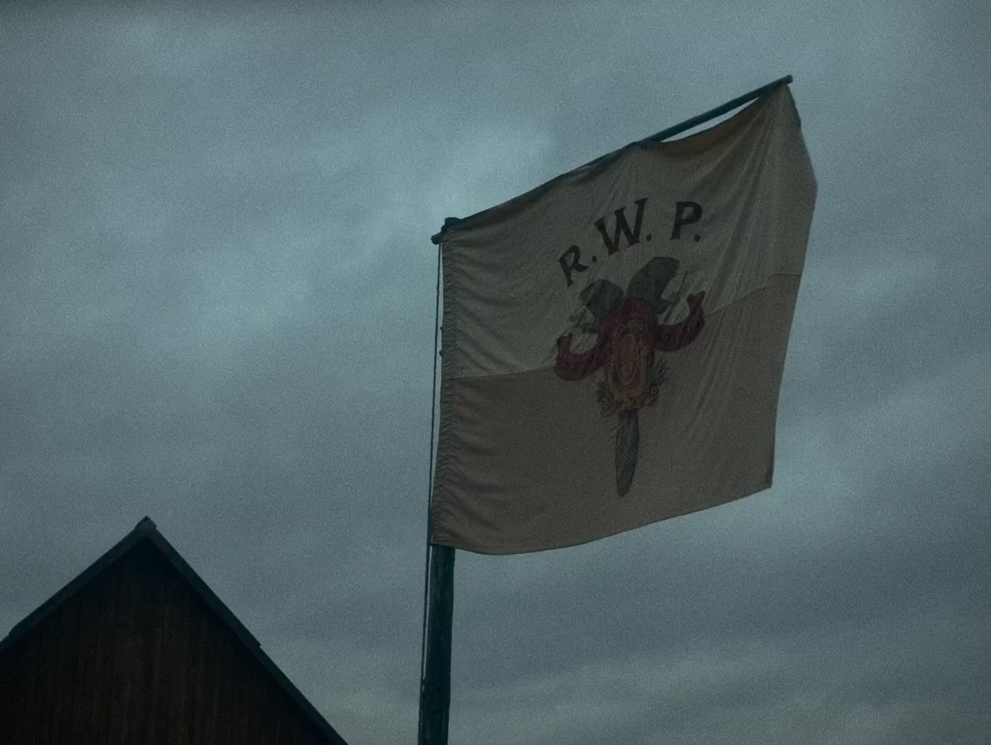 A white flag on a pole against a flat overcast sky above a shingled roof.