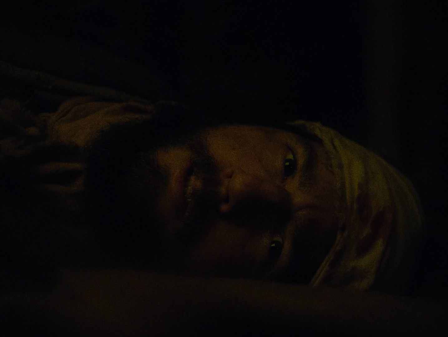A man's face lying on its side, lit warmly by a lamp out of frame.