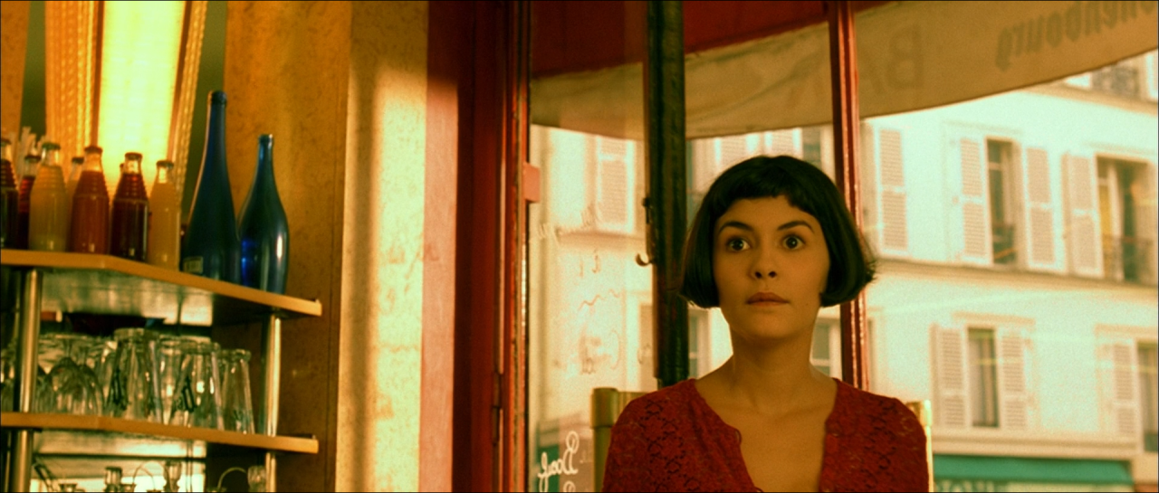 Amélie in a red dress inside a bright café with teal-green fixtures.