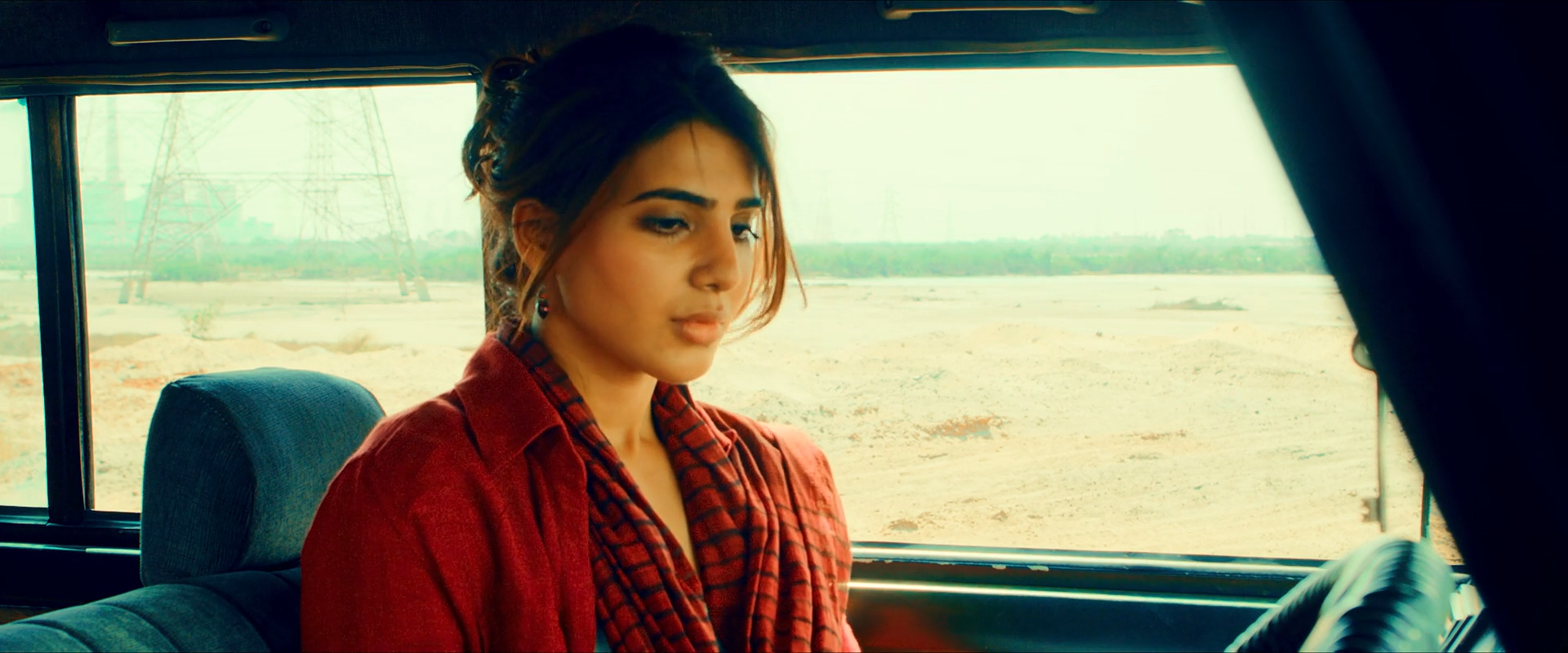 A woman in red sits in a teal car interior, surrounded by very bright salt-flat landscape visible through the windows.