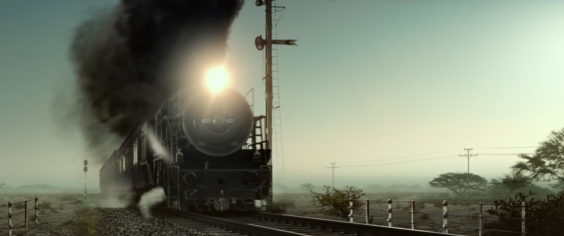 A steam locomotive approaches head-on through a pale green and sepia landscape, trailing a huge mass of black smoke.